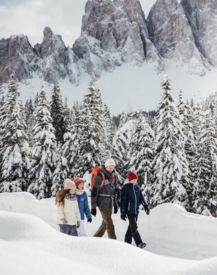 Un uomo cammina nella neve con tre bambini, circondato dalle Dolomiti innevate