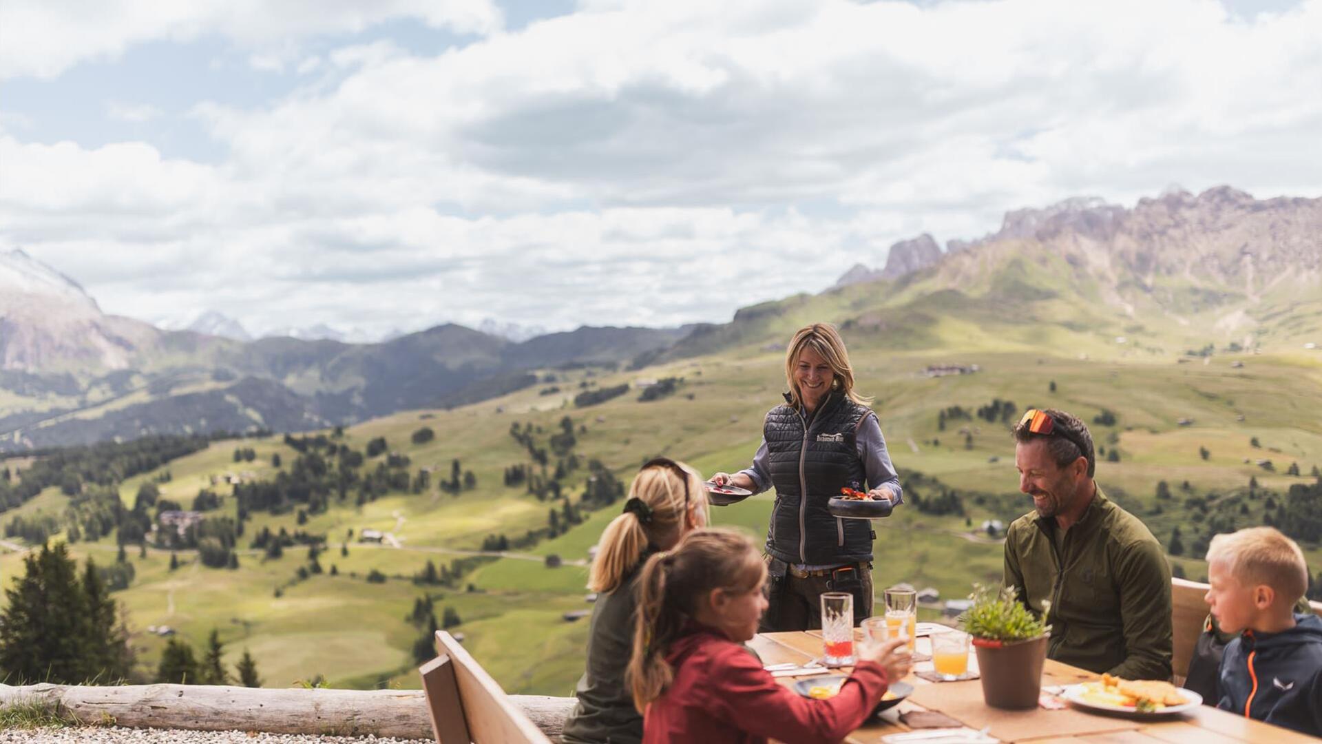 Eine Familie sitzt an einem Tisch und eine Frau serviert ein Gericht
