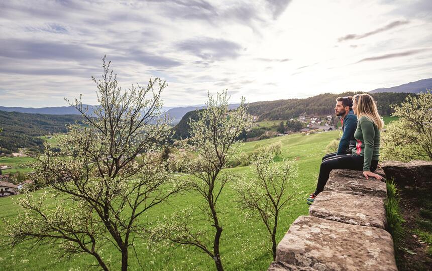 Ein Mann und eine Frau sitzen auf einer Mauer und blicken nach Seis am Schlern