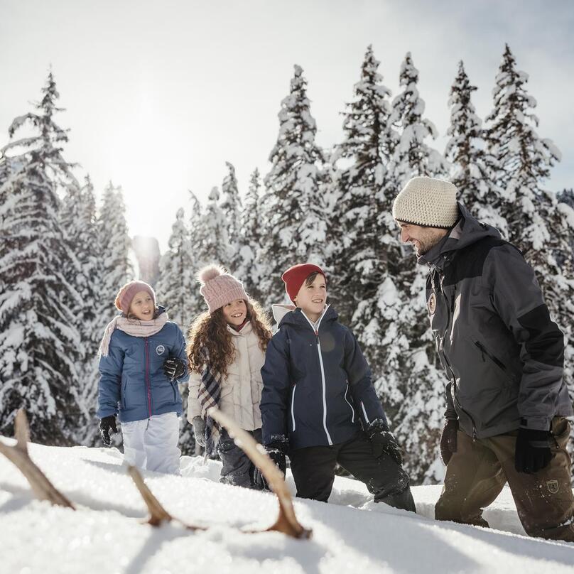 A man is hiking in the snow with three children, surrounded by the snow-covered Dolomites
