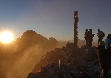 Three people are standing on a summit at sunrise