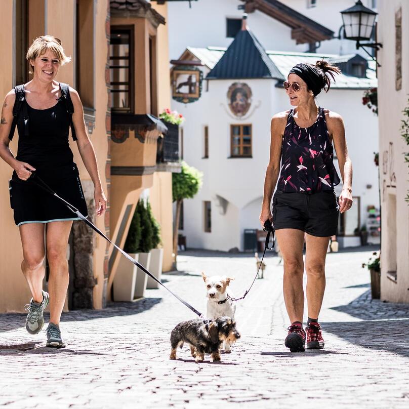 Zwei Frauen gehen mit ihren angeleinten Hunden durch den Ortskern