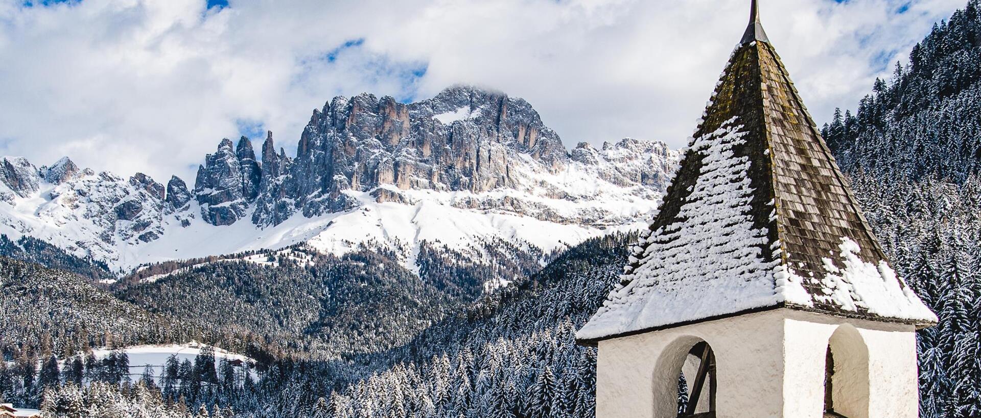 Il campanile di Tires al Catinaccio; sullo sfondo il Rosengarten coperto di neve