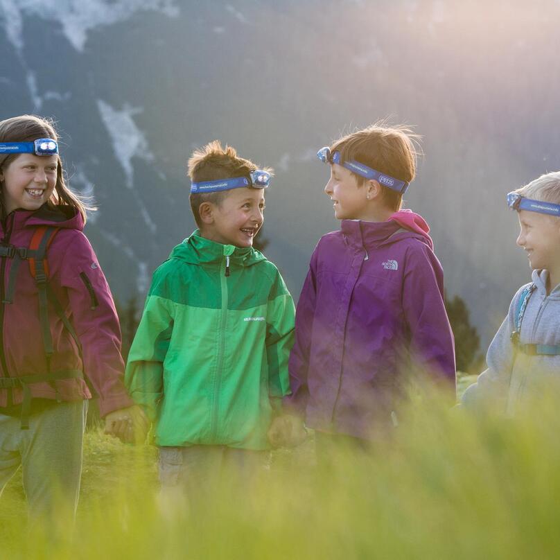 Four children are holding hands and exploring nature with headlamps