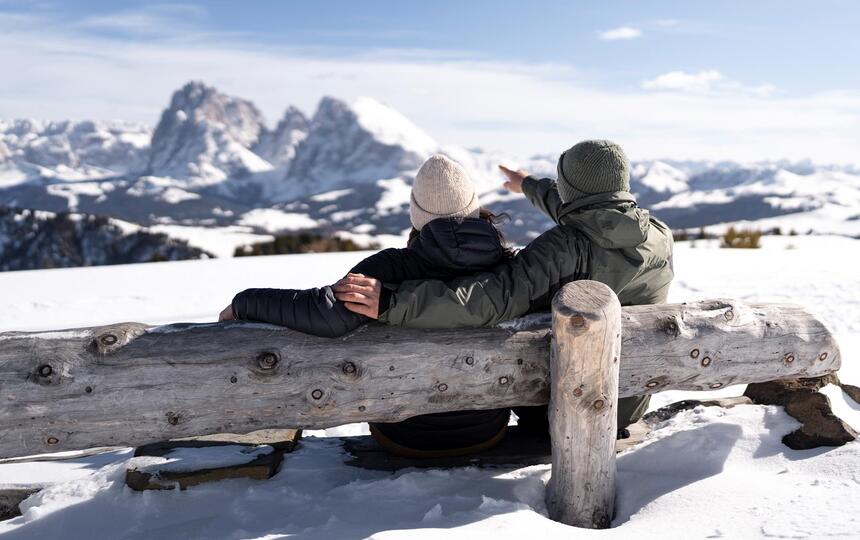 Un uomo e una donna sono seduti su una panchina di legno e guardano le Dolomiti