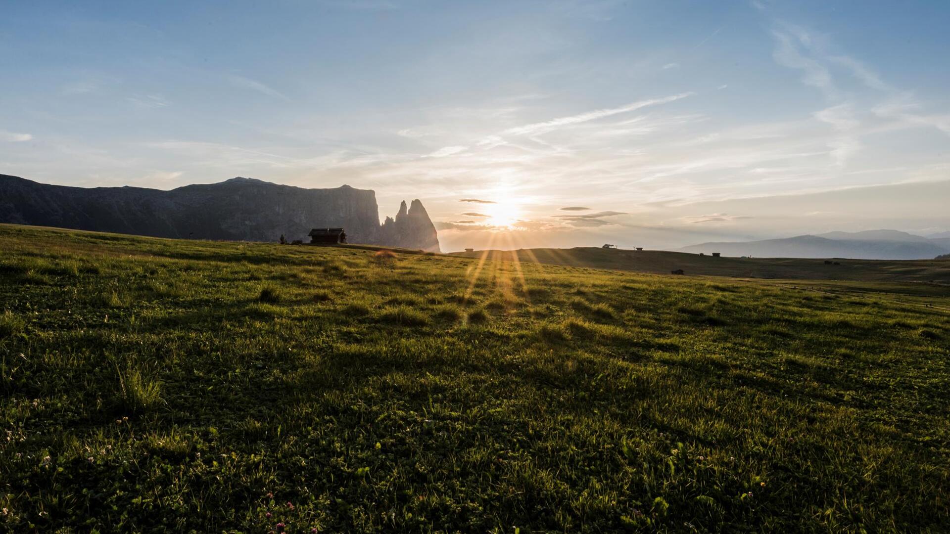 Sonnenuntergang auf der Seiser Alm mit weiten Wiesen und Bergen im warmen Licht