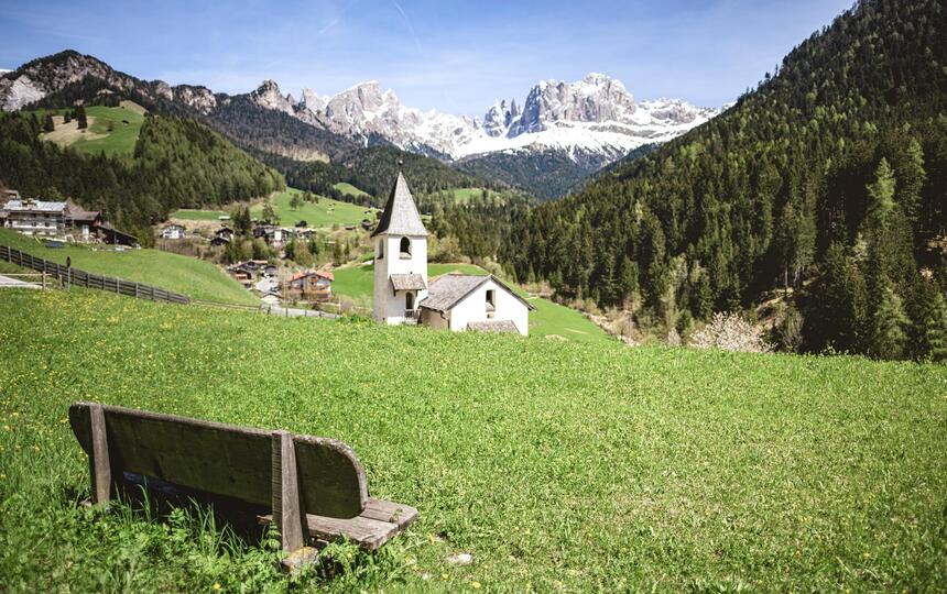 Blühende Wiesen mit  Blumen, im Hintergrund eine kleine Kapelle in ruhiger Landschaft