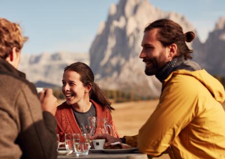 Drei Personen trinken einen Kaffee, im Hintergrund die Dolomiten