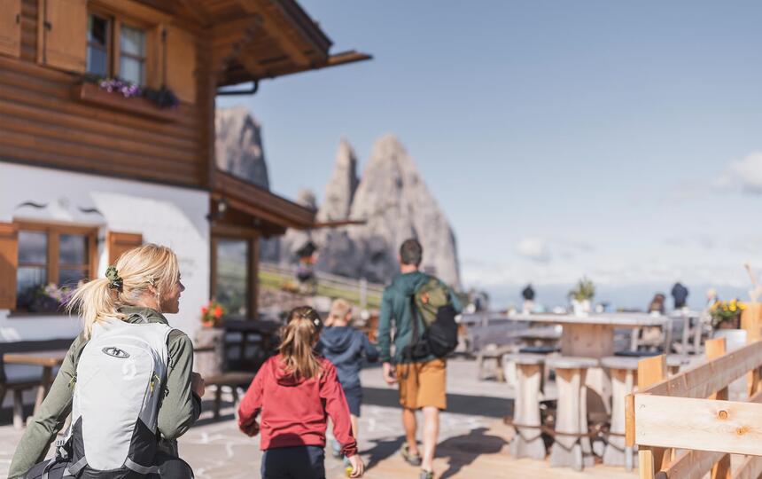 A family with two children stopping at a mountain hut, with the Schlern in the background