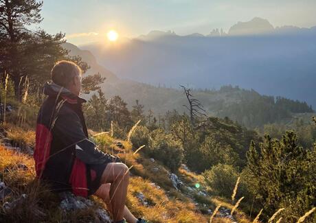 Ein Mann sitzt auf einem Berg und betrachtet den Sonnenuntergang