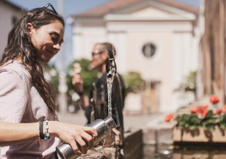 Eine Frau füllt eine Flasche Wasser bei einem Brunnen auf