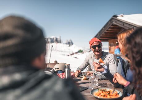 Eine Familie mit zwei Kindern kehrt in einer Hütte ein, im Hintergrund der Schlern