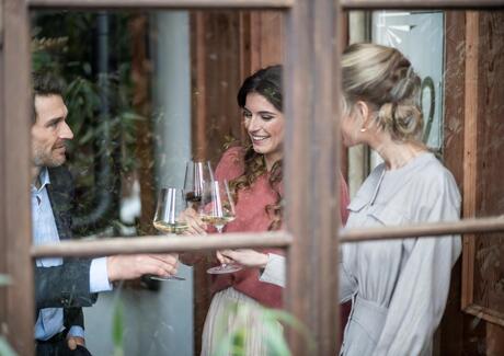 Zwei Frauen und ein Mann stoßen mit einem Glas Wein an