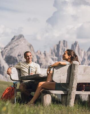 Ein Mann und eine Frau sitzen auf einer Holzbank mit Blick auf die Dolomiten