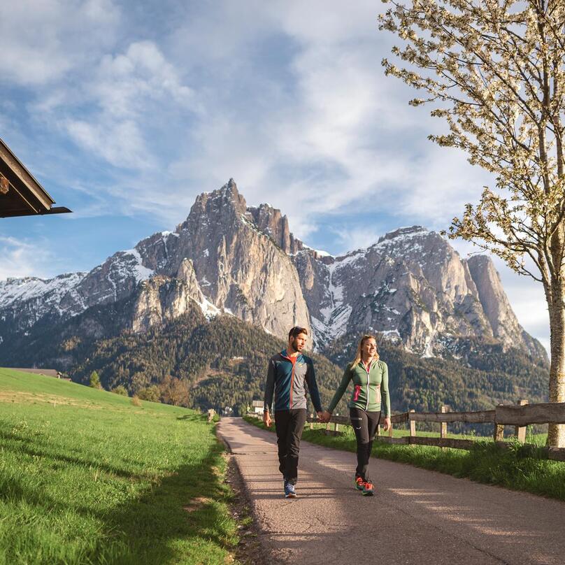 A man and a woman are walking with the Dolomites in the background