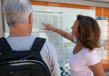 A man and a woman are reading a bus timetable