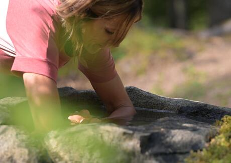 Frau taucht ihre Hände in das Wasser eines steinernen Brunnens