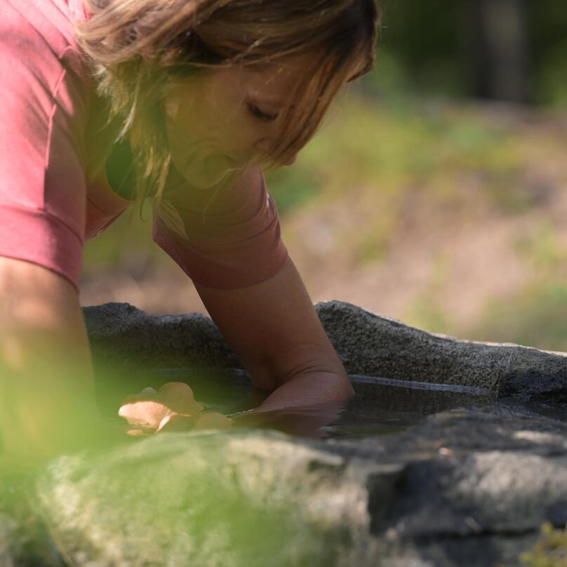 A woman dips her hands into the water of a stone fountain