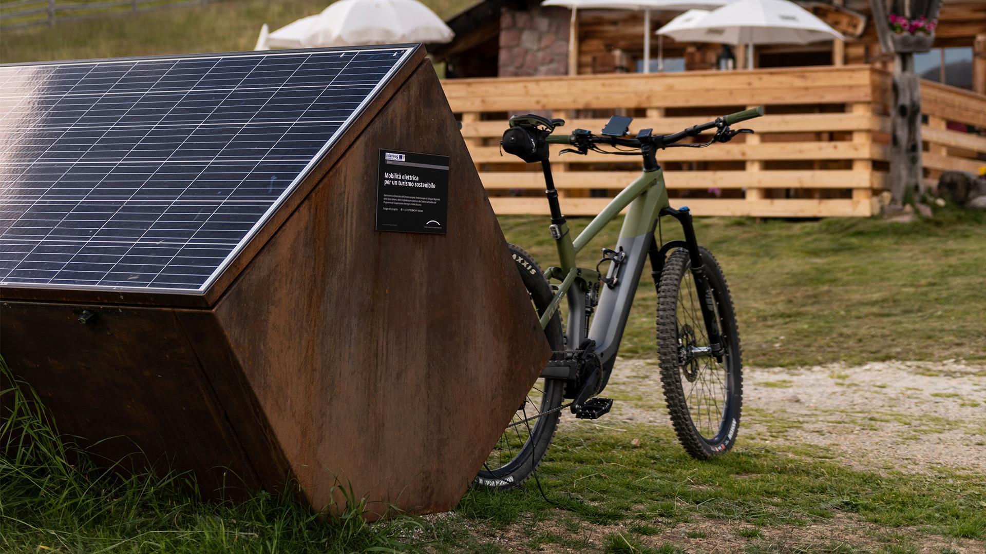 An e-bike is charging at a mobile charging station in front of an alpine hut