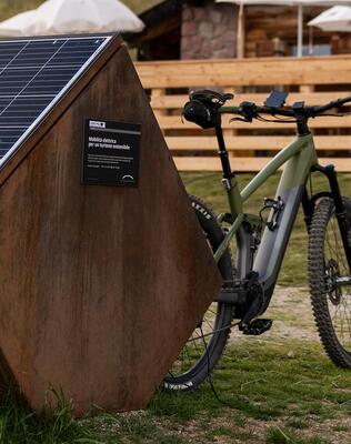 An e-bike is charging at a mobile charging station in front of an alpine hut