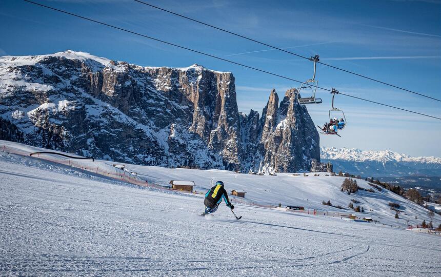 Ein Mann fährt mit einem Monoski die Piste hinunter, im Hintergrund der Schlern