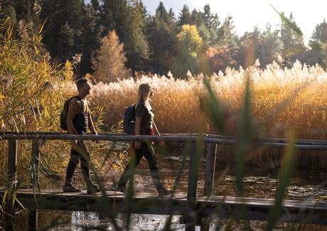 A man and a woman are sitting on a wooden bench, looking toward Völs am Schlern