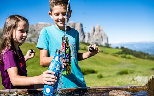 Family holiday in the Dolomites - children at the drinking fountain on the Seiser Alm