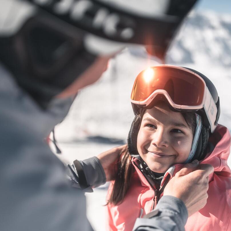 Eine Frau hilft einem Kind beim Aufsetzen eines Skihelms