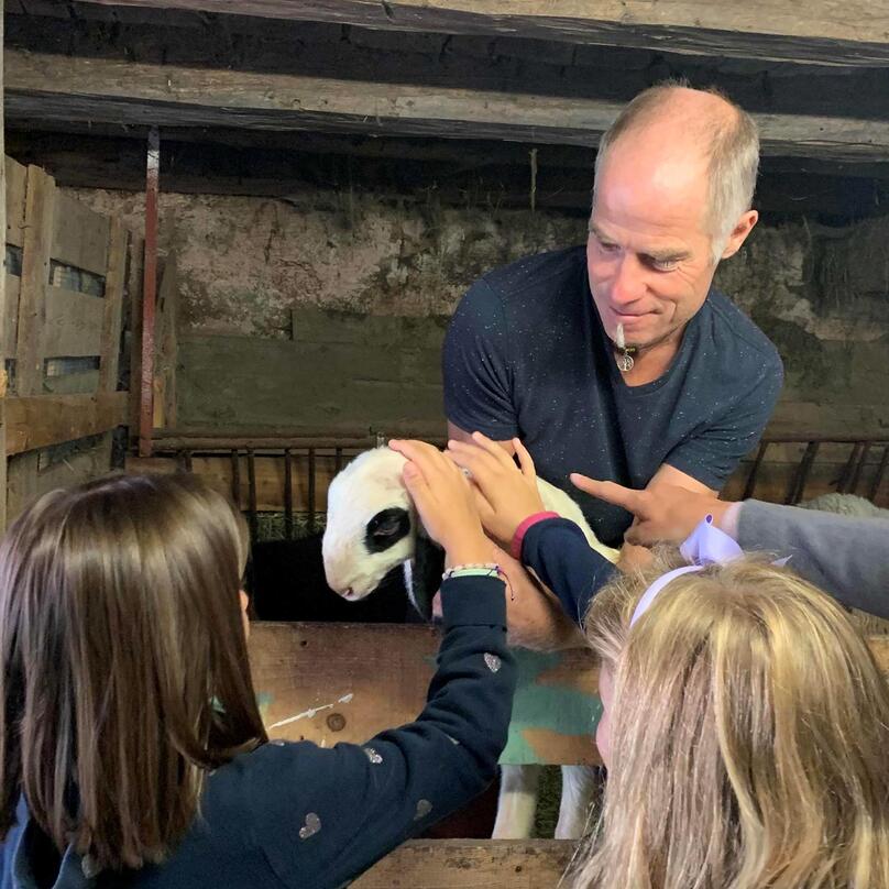 A man is holding a lamb while two children are petting it